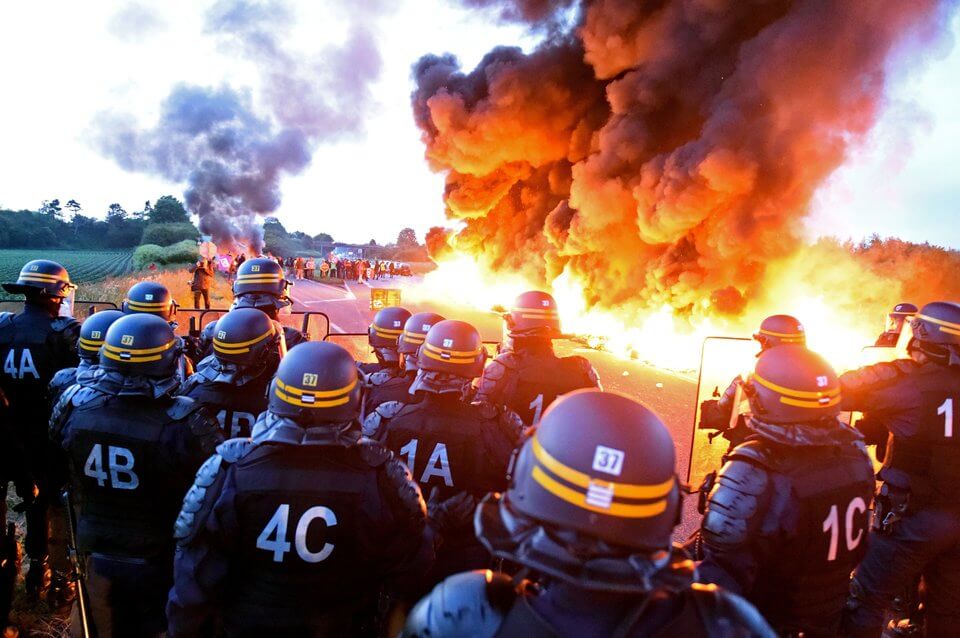 Riot police stand guard behind a fire as refinery workers hold a blockade of the oil depot of Douchy-Les-Mines to protest against the government's proposed labour reforms, on May 25, 2016. Refinery workers stepped up strikes that threaten to paralyse France weeks ahead of the Euro 2016 tournament as the government moved to break their blockades, escalating a three-month tug-of-war over labour reforms. / AFP / François LO PRESTI (Photo credit should read FRANCOIS LO PRESTI/AFP/Getty Images)
